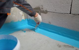 Image shows person applying interior sealants, a common basement waterproofing method.